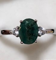 Close-up front view of sterling silver ring with oval emerald and side clear stones.