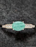 Close-up front view of the sterling silver ring with oval green emerald center stone and diamond accents on the band.