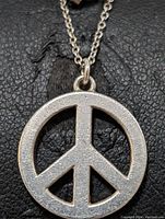 Close-up front view of the round peace sign pendant on sterling silver chain, showing textured matte finish on pendant surface and oval chain links.