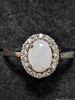 Close-up top view of the sterling silver oval opal ring showing play-of-color and surrounding halo of small clear stones on black background.