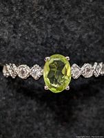 Close-up front view of sterling silver ring with oval peridot gemstone and decorative band.