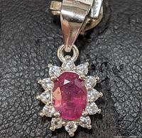 Close-up image showing oval ruby surrounded by small white diamond-like accents mounted in sterling silver pendant