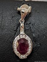 Front view of the sterling silver pendant showcasing the oval ruby surrounded by small clear stones.