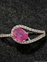Close-up of the sterling silver ring showing oval pinkish-red ruby in center with small clear stones on split shank band.