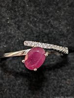 Close-up front view of sterling silver ring showing oval ruby and partial row of small clear stones on band.