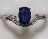 Close-up front view of sterling silver ring with oval blue sapphire and clear accent stones.