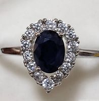 Close-up front view of the sterling silver ring showing the oval sapphire center surrounded by clear CZ stones in a pear-shaped halo.