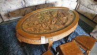 Full view of oval carved wooden coffee table with glass top showing overall design, legs, and surrounding furniture.