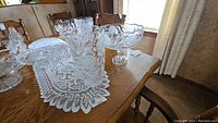 Photo of crystal vase and pedestal bowl arranged on a wooden table with lace tablecloth.