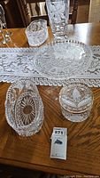 Photo showing crystal jewelry box, oval serving dish, and the round cake stand on a wooden table with a lace runner.