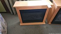 Front view of the portable electric fireplace heater with oak finish on carpeted floor.