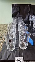 12 clear crystal glasses arranged in two rows on a dark surface, showing the set quantity and design.