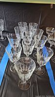 Set of 12 clear crystal wine glasses arranged in rows on black surface with blue tape.