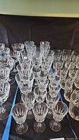 Photo showing multiple clear stemmed crystal glasses with faceted designs, arranged on a black cloth background.