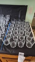 Photo showing front view of 24 clear crystal tumblers arranged in rows on a table.