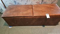 Full view of the rectangular brown leather storage bench with ribbed texture and two cushioned seats on top.