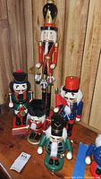 Full view of all five nutcrackers of various sizes and colors on wooden surface against wooden wall