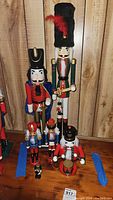 Group photo showing all six wooden nutcrackers arranged by height against a wooden wall background on a wooden surface.