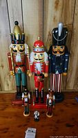 Front view of the six nutcrackers showing their heights and designs on a wooden surface in front of a vertical wooden plank background.