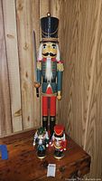 Full view of three nutcrackers, one large and two small, displayed on wooden surface with wood panel background