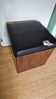 Square storage ottoman with dark brown leather top and wooden base on casters.