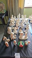 General view showing a variety of Precious Moments figurines arranged on a black surface, including angelic and child figures primarily in pastel shades.