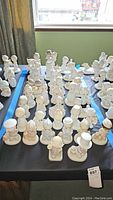 Wide shot of numerous Precious Moments porcelain figurines arranged on a table near a window.