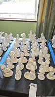 Wide angle view showing multiple Precious Moments figurines arranged on a table, including children and animals in soft colors.