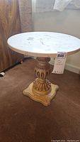 Side view of round side table with plastic top and carved wooden base showing overall condition and design.
