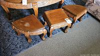 Three wooden carved stools with detailed legs and tops showing surface wear, nested partially under an oval table.