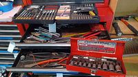 Workbench drawer with assorted hand tools including pliers, wire cutters, punch tools, and Kobalt hex bit socket set in a red metal case.