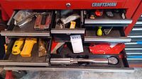 Partially opened Craftsman red tool chest with multiple drawers showing assorted small hand tools including clamps, wrenches and drill bits.