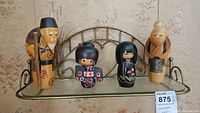 Four wooden dolls displayed on a metal glass shelf, showing full set view
