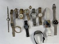 Overview of 13 assorted wristwatches laid out, showing variety in band styles and watch face shapes and colors.