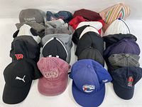 24 assorted baseball caps and trucker hats in various colors and styles arranged on a flat surface.