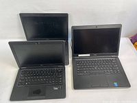 Three Dell laptops displayed with screens and keyboards visible, showing worn condition and no accessories