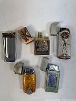 Five assorted collectible butane lighters showing overall conditions and design details.