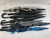 Eight assorted umbrellas arranged horizontally showing various handle styles and colors including white, black, blue, and patterned canopies.