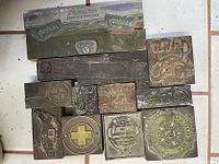Multiple antique printing wood blocks with copper faces arranged on a tiled floor, showing various engraved designs including symbols, text, and emblems.