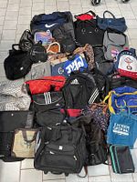 Overview photo showing a selection of assorted pre-owned bags including backpacks, tote bags, duffle bags, and other cases in various colors and brands on a tiled floor.