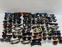 Wide assortment of multiple pairs of men's and women's sunglasses arranged in rows showing variety of frame colors, shapes, and lens styles.