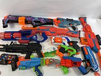 Photo showing 11 assorted toy blasters of varying sizes, colors and brands arranged side by side.