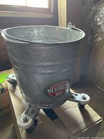 Side view of the galvanized bucket showing Behrens label and caster wheel base