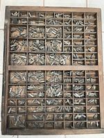 Photo of wooden box with many compartments holding assorted vintage metal letterpress printing letters of various characters.