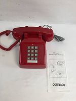 Red Cortelco corded desk phone with keypad and instruction manual