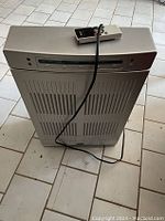 Full front view of silver Dayton air cleaner with vertical vent slats on front panel. Remote control resting on top.