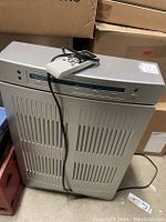 Dayton portable air cleaner showing front vent slats, control panel on top, and remote control resting on top.