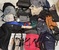 Top-down photo showing various bags including backpacks, tote bags, duffle bags, and cases arranged on floor