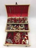 Overview of open jewelry box showing all three compartments filled with assorted fashion jewelry including necklaces, earrings, bracelets and pins.