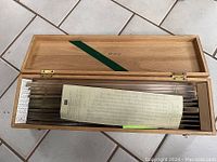 Open wooden case showing architectural drafting tools neatly arranged with a printed reference sheet on top